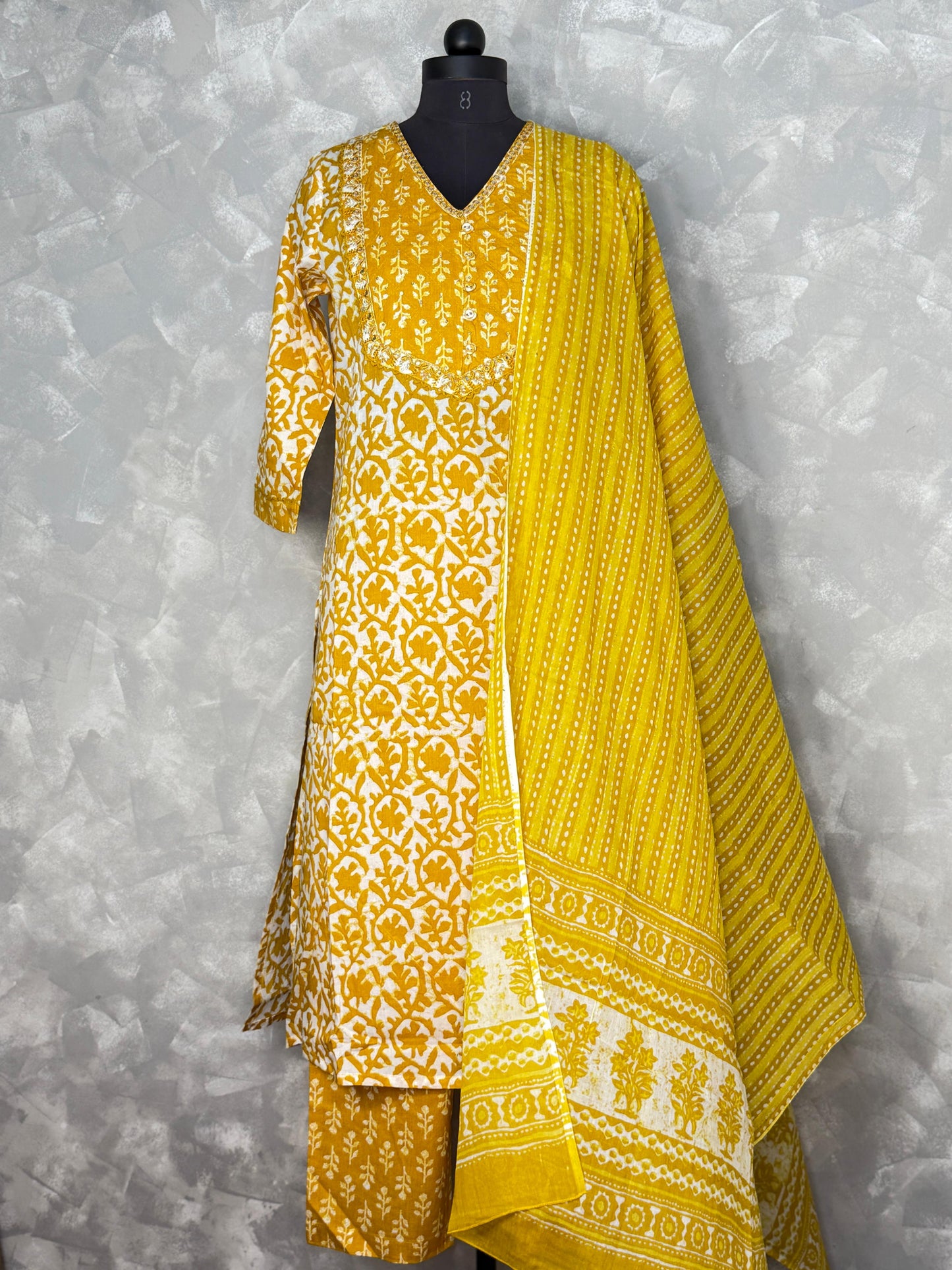 Yellow and white patterned dress on a mannequin against a gray background