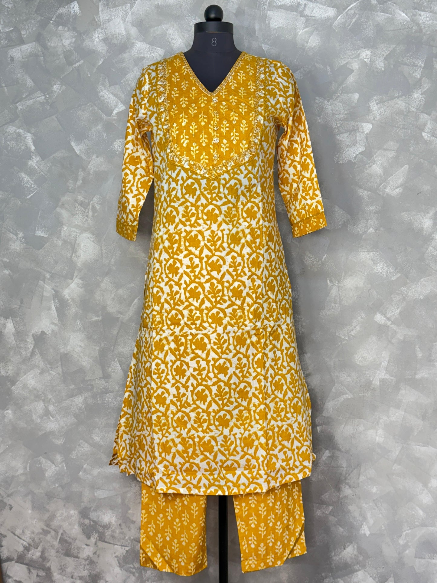 Yellow and white patterned kurta set on a mannequin against a gray background